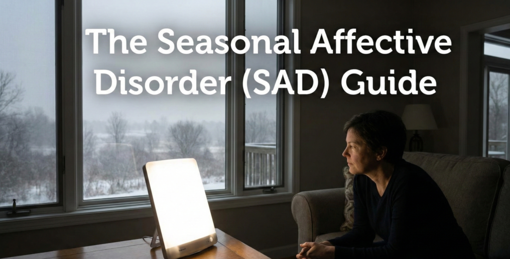 A woman sits in a dimly lit room looking out a window at a snowy winter landscape while a bright light therapy box sits on a table in front of her. The text "The Seasonal Affective Disorder (SAD) Guide" is superimposed at the top.