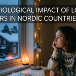 An interior photograph of a woman wearing a traditional Nordic sweater sitting at a desk during a dark winter evening in Scandinavia, looking contemplatively out a snowy window. On her desk are a cup of tea, a bright light therapy lamp (used for SAD), and a psychology textbook. Text overlay at the top reads: "THE PSYCHOLOGICAL IMPACT OF LONG, DARK WINTERS IN NORDIC COUNTRIES (SAD)".