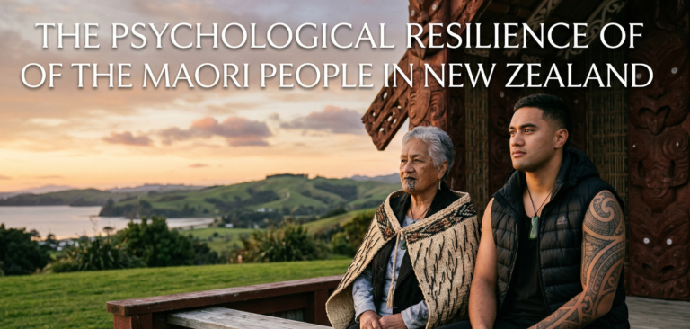 Photograph of an elder Maori woman with a moko kauae and a young Maori man with arm ta moko, sitting together on a bench. They are outside a carved wharenui (meeting house) with a coastal New Zealand landscape at sunset. White text at the top reads: 'THE PSYCHOLOGICAL RESILIENCE OF THE MAORI PEOPLE IN NEW ZEALAND'.
